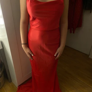 Röd långklänning - Snygg röd långklänning med smala axelband och en elegant draperad urringning. Perfekt för en festlig kväll. Klänningen har en figurnära passform som framhäver silhuetten.
