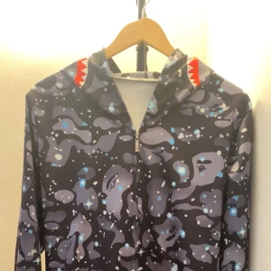 Mönstrad hoodie med hajmotiv - Säljer en cool hoodie med ett unikt mönster i grått, blått och vitt. Hoodien har ett hajmotiv på huvan och dragkedja framtill. Perfekt för dig som vill sticka ut! Pris kan diskuteras det är ba och skriva så sänker jag!