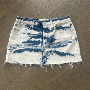 Blå och vit lågmidjad jeanskjol från Jeanerica - Snygg lågmidjad jeanskjol från Jeanerica i en cool blå och vit batikstil. Kjolen har en klassisk femficksdesign och en kort längd som ger en trendig look. Perfekt för att ge din outfit en unik touch! midjemått 37 cm rak över
