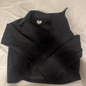 Svart/grå kappa från Kappahl - Säljer en stilren svart kappa från Kappahl i storlek M. Den har en klassisk design med knappar framtill och en elegant krage. Perfekt för kyligare dagar och ger en sofistikerad look.