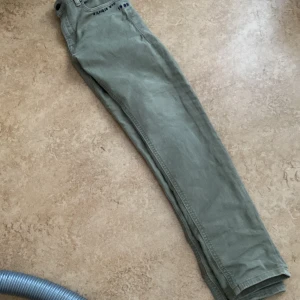 Gröna byxor från Tommy Hilfiger - Snygga grågröna byxor från Tommy Hilfiger med klassisk design. Byxorna har en rak passform och är tillverkade i ett slitstarkt material. De har två bakfickor och en diskret logga på baksidan. Perfekta för en stilren look.