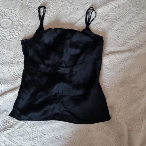 Svart satinlinne från Zara - Snyggt svart linne i satin från Zara med tunna axelband och en elegant drapering framtill. Linnet har en en blandning av sprts och satin framtill vid brösten. Som syns på bilderna. 