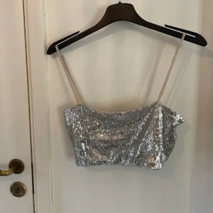 Glittrig silver tubtopp - Snygg glittrig tubtopp i silver med smala axelband. Perfekt för en festlig kväll eller nyårsfirande. Toppen är croppad och täckt med paljetter som ger en glittrande effekt.