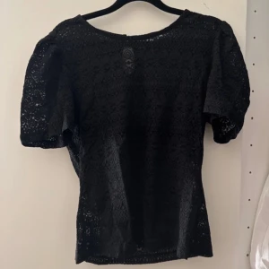 Svart spetsblus - Elegant svart spetsblus med korta ärmar och ett vackert mönster. Perfekt för att ge en stilfull touch till din outfit.