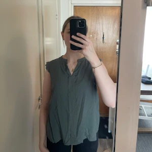 Grön ärmlös blus från Only Carmakoma - Säljer en stilren grön ärmlös blus från Only Carmakoma. Blusen har en enkel design med spetsdetaljer vid ärmhålen och en diskret knäppning framtill. Perfekt för en avslappnad men ändå elegant look.