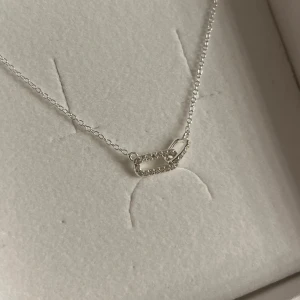 Silverhalsband med säkerhetsnål-design - Elegant silverhalsband med en unik säkerhetsnål-design. Kedjan är tunn och smidig, vilket ger ett stilrent intryck. Perfekt för att ge en subtil men trendig touch till din outfit.