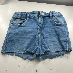 Blå jeansshorts från Name It - Säljer ett par snygga blå jeansshorts från Name It. De har en fransig kant och klassisk femficksdesign. Passar på barn även under 14 år.