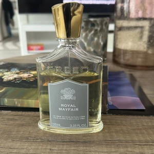Royal Mayfair parfym från Creed - Exklusiv parfymflaska på 100 ml från Creed med doften Royal Mayfair. Flaskan har en elegant design med en gyllene kork och en grå etikett med vit text. Perfekt för den som söker en lyxig och sofistikerad doftupplevelse. Ny pris 3500, använd 15-20 ml. Pris 2600