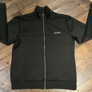 Svart tröja med dragkedja från Les Deux - Snygg mörk grön tröja från Les Deux med dragkedja framtill. Tröjan har en hög krage och två fickor på framsidan. Helt ny, användt den 3 gånger. Perfekt för en stilren look.