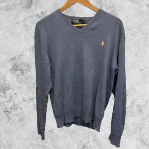 Ljusblå tröja från Polo Ralph Lauren - Säljer en stilren ljusblå tröja från Polo Ralph Lauren i 100% pima bomull. Tröjan har en v-ringad design och ett litet broderat logotypmärke på bröstet. Perfekt för en klassisk och avslappnad look.