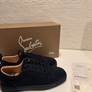 Mörk blåa sneakers från Christian Louboutin - Snygga mörk blåa sneakers från Christian Louboutin med den ikoniska röda sulan. Skorna har en stilren design med snörning och är perfekta för en trendig look.
