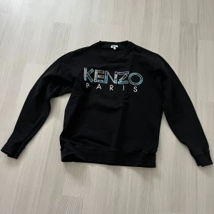 Svart sweatshirt från Kenzo - Snygg svart sweatshirt från Kenzo med deras ikoniska logga i färgglada bokstäver på bröstet. Tröjan har långa ärmar och en klassisk rund halsringning. Perfekt för en stilren och avslappnad look.