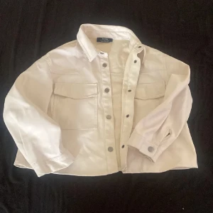 Vit trekvartsärmad skinnjacka/skjorta från Bershka - Snygg vit skinn trekvartärmad jacka/skjorta från Bershka med knappar framtill och två bröstfickor. Jackan har en klassisk krage. Perfekt för en stilren look. Super snygg till våren❤️