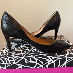 Svarta pumps från Diane von Furstenberg - Eleganta svarta pumps i skinn från Diane von Furstenberg med en spetsig tå och klack. Skorna har en texturerad yta som ger en lyxig känsla. Perfekta för en stilren look. I storlek 38. Använda en gång. 