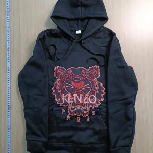 Svart hoodie från Kenzo - Snygg svart hoodie från Kenzo med ett coolt tigertryck i rött och rosa på framsidan. Tröjan har en klassisk känguruficka och justerbar huva med snören. Perfekt för en avslappnad stil.