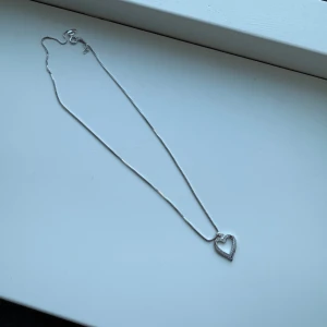 Silverfärgat halsband med hjärthänge - Elegant silverfärgat halsband med ett hjärthänge. Perfekt för att ge en subtil glans till din outfit. Kedjan är tunn och smidig, vilket gör den bekväm att bära hela dagen.