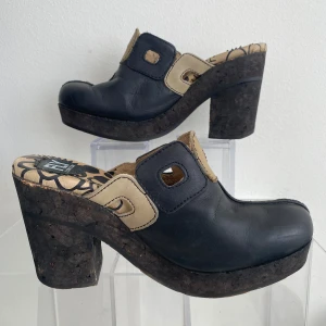 Svarta klackskor från Fly London - Snygga svarta klackskor från Fly London med beige detaljer och en unik mönstrad innersula. Skorna har en hög klack och en öppen häl, vilket ger dem en modern look. Såå snygga, ett måste till sommarens look! 