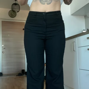 Svarta kostymbyxor från Monki - Snygga svarta kostymbyxor med hög midja och rak passform. Perfekta för en stilren look. Byxorna har en klassisk design med knappar framtill. Från Monki. Kortare i passformen. Jag är 165 cm. 