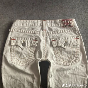 Lågmidjade bootcut True religion jeans - Tryck gärna på ”köp”!💗 Snygga lågmidjade vita True religion jeans med gula/orange stygn! Dom är bootcut/flare och i storlek 27. Midjemått ca 37 Innerbenslängd ca 74. Har en grå fläck på vänstra lår, se bild 5! Annars toppskick!💕 jag är 165