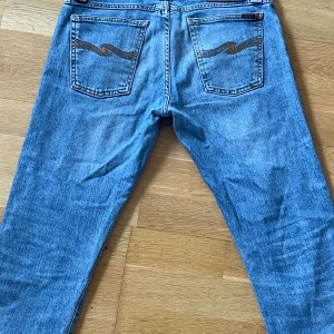 Nudie Jeans - Säljer ett par snygga blåa nudie jeans med broderade detaljer på bakfickorna. De har en klassisk straight passform och är perfekta för vardagsbruk. Jeansen är i 9/10 skick och har en bekväm midwaist. Perfekta för både höst och vår! Storlek W30 L30, skicka om ni har några funderingar och priset är inte ristat i en sten går och förhandla
