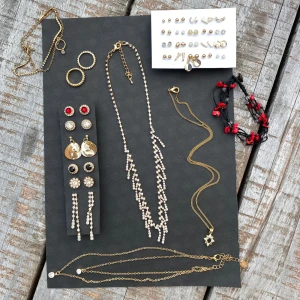 Samling av smycken ALTT INGÅR DU FÅR ALLT PÅ BILDEN - En fantastisk samling av smycken som inkluderar flera par örhängen, halsband och armband. Örhängena har olika stilar, från stora guldplattor till glittriga stenar i både röda och svarta toner. Halsbanden är dekorerade med pärlor och har eleganta kedjor i guld. Det finns också ett armband med röda och svarta detaljer. Perfekt för att lysa upp vilken outfit som helst!