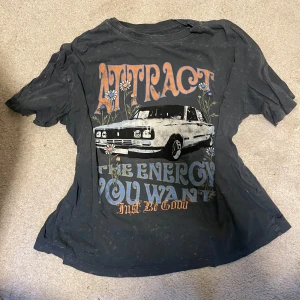Svart t-shirt med biltryck - Jättecool svart/grå t-shirt med ett vintageinspirerat tryck av en bil och texten 'Attract the energy you want'. T-shirten har korta ärmar och är oversized i passformen. Perfekt till hösten!