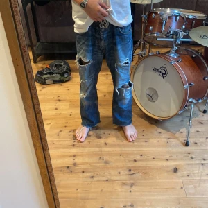 Blå slitna jeans från RDWD - Säljer ett par blå jeans från RDWD med en riktigt cool, sliten look. De har stora hål och slitningar på knäna och låren, vilket ger dem en avslappnad och trendig stil. Perfekta för en casual outfit. De är i en baggy passform men är ganska korta. Personen på bild är 183 cm