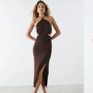 Brun satinklänning - Brun satinklänning med halterneck, cutout vid sidan av midjan, slits, och öppen rygg. Midi/maxi lång. Använd 1 gång, därav i mycket bra skick. Perfekt till fest, men går även att använda till en sommardag med ett par tofflor!  Ordinarie pris: 599 kr