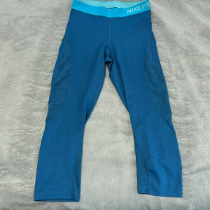 Nike Pro tights - Träningstights från Nike Pro. Storlek S men kan även användas av M om man gillar tightare. Mörkturkos färg med ljusblå rem i midjan. Fina detaljer med håligt material utmed benen och en ljusblå swoosh på baksidan av ena benet. I mycket gott skick!