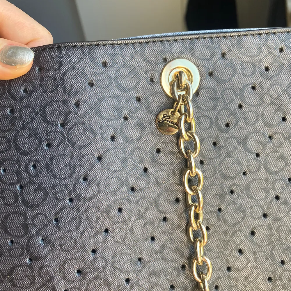 Svart handväska från Guess med gulddetaljer. I använt skick. Har dragkedjeficka och fack.. Väskor.