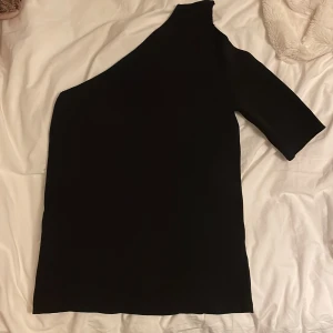 Svart asymmetrisk topp - Svart asymmetrisk topp från chiquelle. Den har ett hål i armen (se bild 2) vilket är tanken. Aldrig använd och har lappen kvar.
