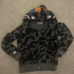 Grå bape hoodie - Säljer nu en fin grå bape hoodie, den är i bra skick inget är trasigt bara att man måste vara försiktig med zippern, eller dra up den långsamt. Det står att den är storlek L men den passar mig som är ca 170 cm.