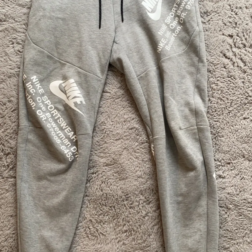 Grå Nike tech byxor med vit text (gammal modell) knappt använd i storlek S. Jeans & Byxor.