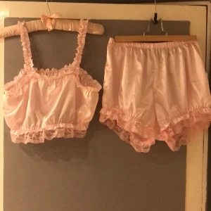 Set top/bralette och mamelucker (laxrosa) oanvänt str L - Rosa/laxrosa  mjukt satintyg med resår i axelband, midja top, och upptill top liksom i midja och benslut byxa. Omkrets top byst 90-120, längd top 24 cm men kan bli längre om du drar i axelbanden. Byxa omkrets midja 72-120 cm, omkrets benslut 52-80 cm