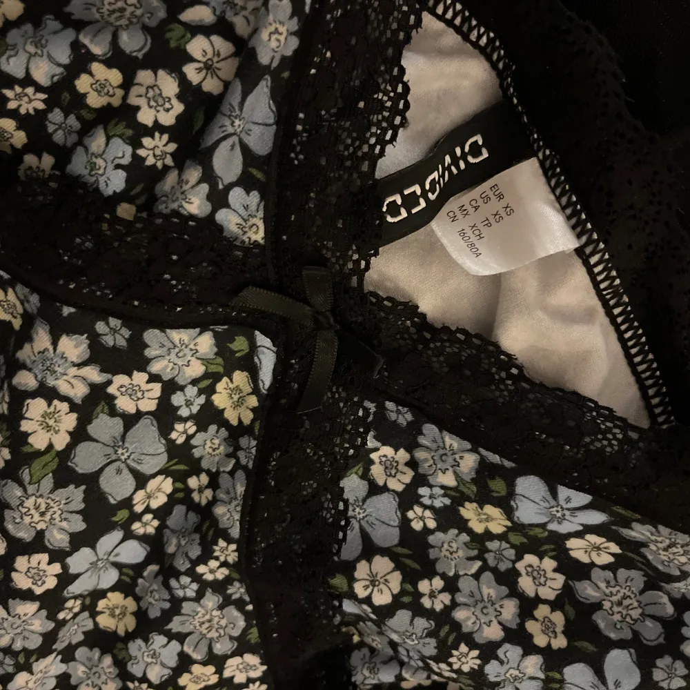 En kort figursydd klänning med blommor och spetsdetaljer upptill och nedtill samt en rosett framtill. Från H&M i strl XS!. Klänningar.