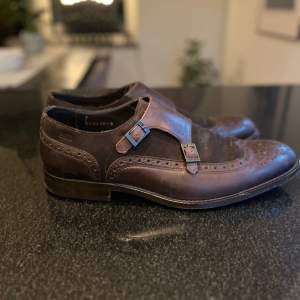 Boss COLBY MONK tillverkade i Italien i blandning av brunn skinn och mocka. Fantastiskt sköna skor, sparsamt använda. Modellnummer 20659088.  Storleken är 7 1/2 vilket motsvara 41 1/2 men kan även användas av dem som har storlek 42.  Innermått 28,2 c