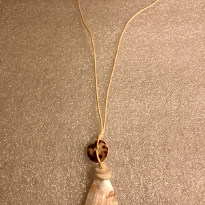 *NY*Längre halsband  - Oanvänt, längre halsband med läderrem och detaljer i trä, berlocken är i plast. På baksidan finns ett litet märke efter prislappen annars inget att anmärka på. 