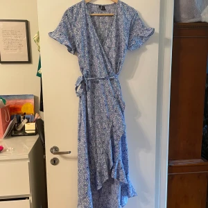 Somrig omlottklänning - En somrigt lila/blå/blommig omlottklänning i storlek S från Veromoda. En extra härlig detalj är klänningens botten där den har olika längd på fram och baksida som skapar ett häftigt flow. Endast använd vid enstaka tillfällen. 