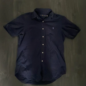 Ralph lauren kortärmad skjorta - Den här skjortan är marinblå och kostade 1499 men jag kommer sälja den mycket billigare och jag har aldrig använt den därför är den i nyskick🥂 Den passar både S och M och den är väldigt skön att ha på sommaren🔥 Hör gärna av er vid minsta fundering🌟