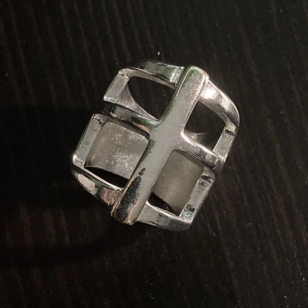 Silverfärgad ring med ett kors, finns visst slitage främst på baksidan av ringen. Innerdiameter: 18 mm, längd: 2,6 cm.. Asusteet.