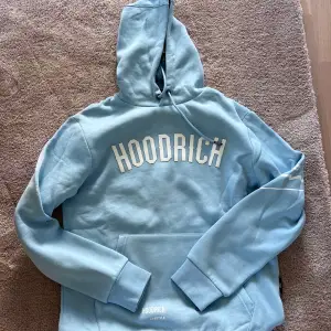 Säljer ett set med en hoodie och byxor från märket Hoodrich. Hoodien har en stor logga på framsidan och texten 
