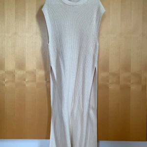 Lång stickad väst - Lång stickad väst som har två slitsar på vardera sida. Går ungefär till mitten av vaden.