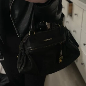 Miu Miu väska - Säljer nu min fina fina Miu Miu väska jag fick ärva ifrån min mamma pga att den inte kommer till användning.   Den är i fint skick!!  Fina guld detaljer på väskan och svart läder!  Skriv privat för fler bilder & info  Pris kan diskuteras 🫶🏼