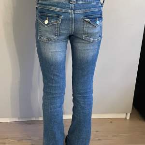 Blåa lågmidjade jeans med två knappar där fram, och fickor med knappar där bak, bootcut jeans, går att spänna in jeansen!