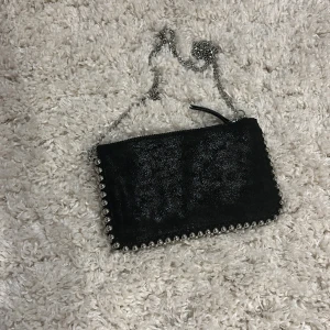 Svart väska  - Liten svart väska från Zara. Väskan har silver detaljer och en avtagbar kjedja. Väskan har inte använt särskilt mycket och är i bra skick. Väskan är liten och har tre fack inuti var av en är med dragkedja.