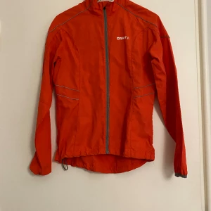 Träningsjacka från Craft - Träningsjacka från Craft, orange/grå. Liten fläck vid nacken, men går säkert bort i tvätten. Dragsko så du kan välja om du vill ha den kortare.