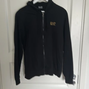 EA7 kofta (svart) - Svart EA7 kofta med guldiga detaljer, allmänt bra skick, lite övertvättad. 