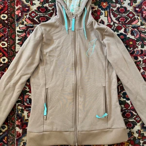 Kofta - cool brun-blå kofta med blommigt mönster i luvan. Köpt secondhand men knappt använd och varan är i nyskick. Stl L men tycker den sitter mer som en M 