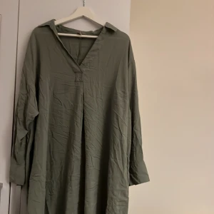 Militärgrön klänning - Skjortklänning i militärgrön. Knappt använd. Väldigt härligt material. Perfekta strandklänningen! Väldigt skrynklig på bild då den legat i garderoben men kan bara strykas eller tvättas och hängas upp! Något längre bak än framtill 