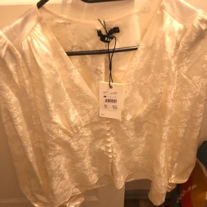 Satin blus - Säljer en jättefin oanvänd satinblus från bik bok! Den är vit med ett mönster av blommor🫶🏽 Den har aldrig kommit till användning då den är lite stor vid bysten. ⚠️ Bild 2 har jag endast med för att visa modellen! 
